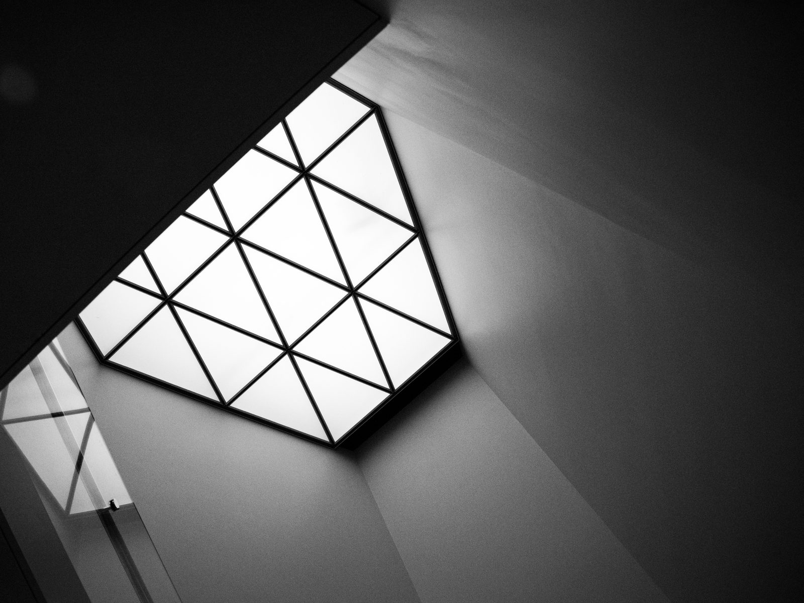 A triangulated glass skylight set into a dark angular ceiling, lit from above.