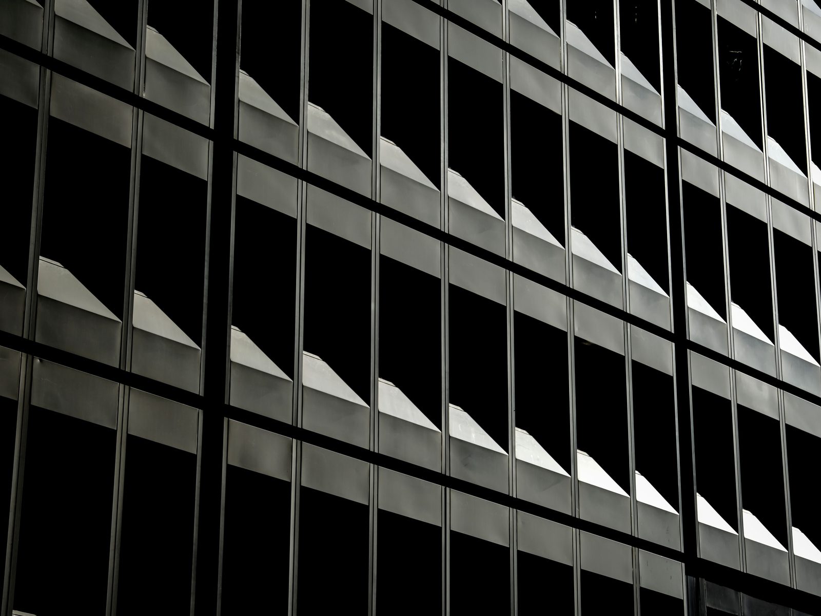 Repeating window bays across a dark glass office facade, each catching a wedge of light.