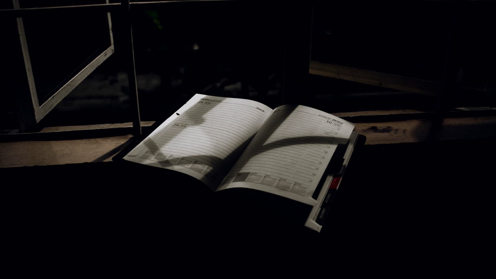 An open planner catching a shaft of window light in a dark room.