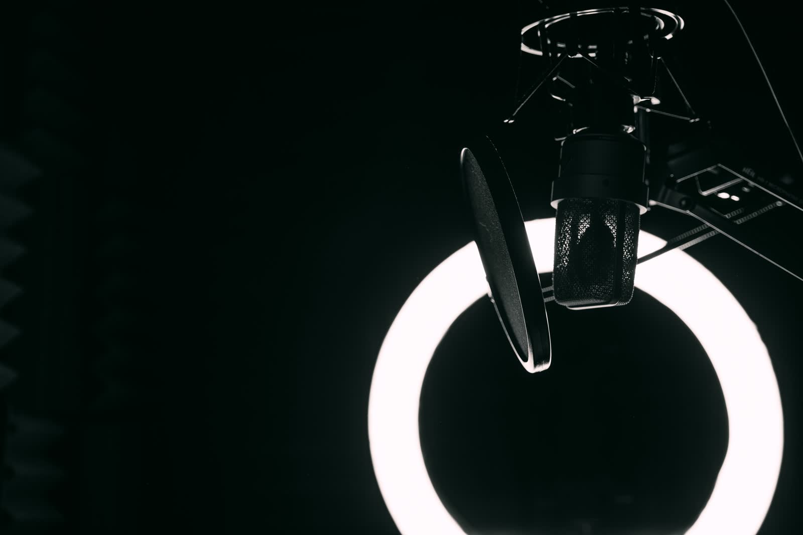 A studio microphone and pop filter lit by a ring light against black.